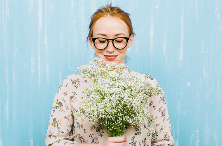 Stocksy-bonninstudio-woman-holding-flowers-in-front-of-blue-background